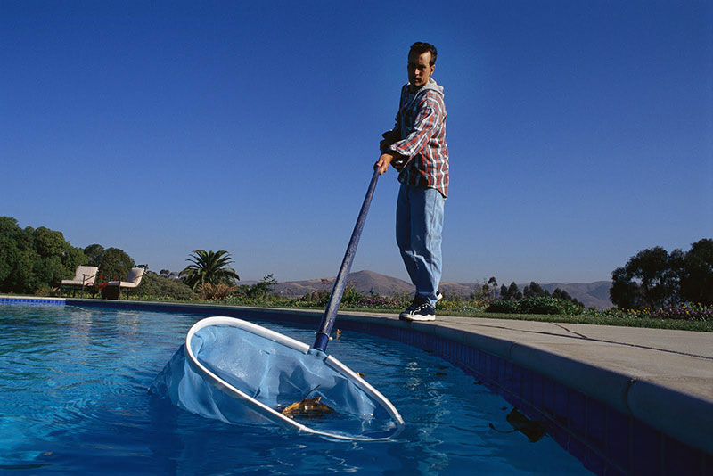 Un operatore pulisce la superficie della piscina con un retino 